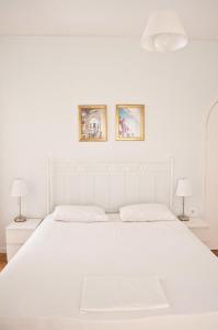 Nikoleta Rooms في تينوس تاون: سرير أبيض في غرفة نوم بيضاء فيها مصباحين