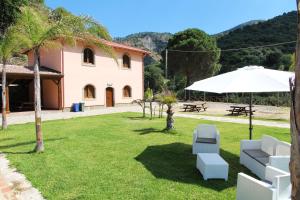 a lawn with a white umbrella and chairs and a building at Profetina Village in Motta Camastra