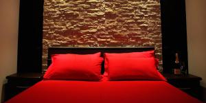 1 cama roja con 2 almohadas rojas frente a una pared de ladrillo en B&B La Bouganville, en Alghero
