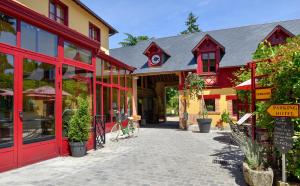 a building with red doors and a street with plants at Logis Hotel La Diligence in La Ferté-Saint-Cyr
