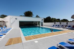 uma piscina com cadeiras azuis e uma pessoa na água em Résidence Prestige Odalys Le Domaine des Pins em Noirmoutier-en-l'lle