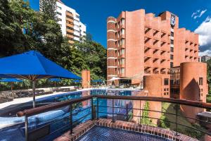 a swimming pool with an umbrella and some buildings at Hotel Dann Carlton Belfort Medellin in Medellín