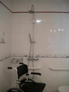 a white tiled bathroom with a chair and a shower at Chambre d'hôte Au col de Cygne in Blanzac-lès-Matha