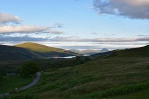 a winding road through a grassy hill with a lake at Killoran House in Dervaig