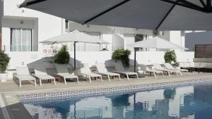 a pool with white chairs and umbrellas next to a pool at Aparthotel Fleming 50 - Adults Only in San Antonio