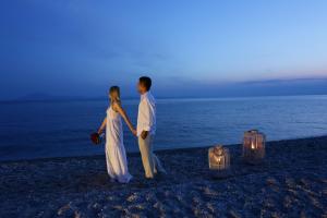 a man and a woman standing on a beach with lights at Alexandra Beach Spa Resort in Potos