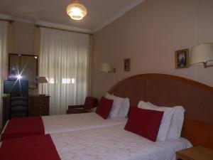 Habitación de hotel con cama con almohadas rojas y blancas en Hotel Larbelo en Coímbra