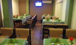 a dining room with green tables and chairs and a tv at Queens Tourist Home in Badagara