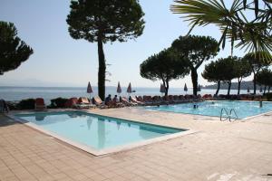 a swimming pool with people sitting in chairs near the ocean at Le Corti Del Lago in Padenghe sul Garda