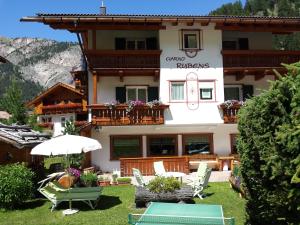 a building with chairs and an umbrella in front of it at Garni Rubens B&B in Selva di Val Gardena