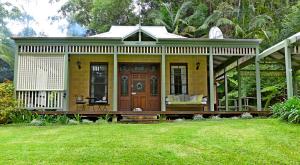 une petite maison jaune avec une terrasse couverte sur une pelouse dans l'établissement Mount Browne Cottage, à Coffs Harbour