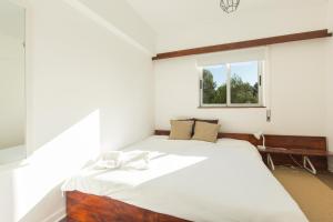 a bedroom with a large white bed with a window at Carcavelos Beach Apartment in Cascais
