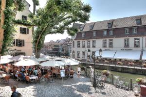 a group of people sitting at tables with umbrellas near a river at Appartement Le bain aux plantes in Strasbourg