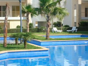 a swimming pool with palm trees in front of a building at Perle de Tamaris in Dar Bouazza