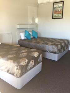 two beds in a hotel room with blue pillows at The Argent Motel in Broken Hill