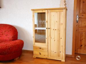 une armoire en bois assise à côté d'une chaise rouge dans l'établissement Haus Kandelblick, à Furtwangen im Schwarzwald