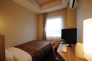 a bedroom with a bed and a desk with a television at Hotel Lexton Tanegashima in Nishinoomote