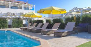 un grupo de sillas y sombrillas junto a una piscina en Quinta Da Rosa Linda, en Monte Gordo