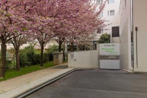 un bâtiment avec un parking avec des arbres aux fleurs roses dans l'établissement Campanile Paris 19 - La Villette, à Paris