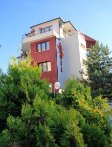 ein rot-weißes Gebäude mit Bäumen davor in der Unterkunft Coral Guest House in Obsor