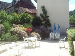 un patio avec des chaises et des tables blanches et un bâtiment dans l'établissement LOGIS HOTEL Les Tilleuls, à Saint-Cirgues-de-Jordanne