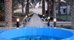 a swimming pool with a fountain in a resort with palm trees at The Pearl Farm Chalet in Barka