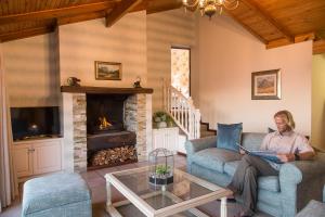 una mujer sentada en un sofá en una sala de estar con un ordenador portátil en The Fernery Lodge & Spa, en Stormsrivier