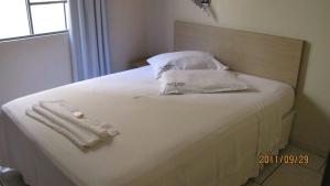 uma cama com almofadas brancas e toalhas em Hotel Joia em Cascavel