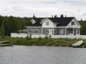 a white house with a white fence and a boat on the water at Miekojärvi Resort in Pello
