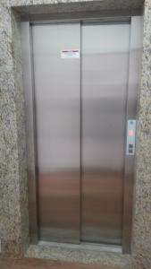 Um elevador de metal num edifício com um sinal. em Hotel Anjos LTDA em Gravataí