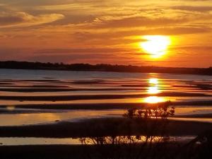 una puesta de sol sobre un cuerpo de agua con olas en Blue Spruces Cottages, en Hampton 