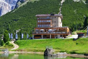 un gran edificio en una colina junto a un lago en Hotel Pordoi Passo Pordoi Vegetarian Hotel en Canazei