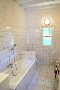ein weiß gefliestes Bad mit einer Badewanne und einem Fenster in der Unterkunft Les Hauts de Chaume in Génillé