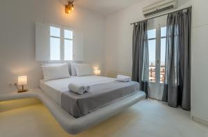 a white bedroom with a large bed and a window at Plaka Suites in Plaka Milou