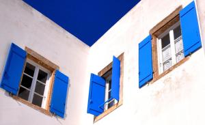 two windows with blue shutters on a white building at Margarita Hotel in Kythira
