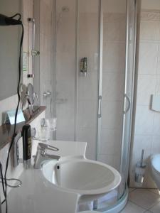 a white bathroom with a shower and a sink at Apart Hotel Norden in Norden