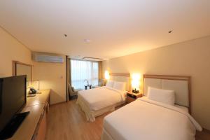 a hotel room with two beds and a flat screen tv at Ocean Suites Jeju Hotel in Jeju