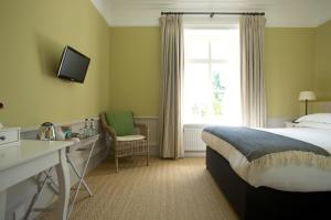 a hotel room with a bed and a desk and a window at The Manor at Sway – Hotel, Restaurant and Gardens in Sway