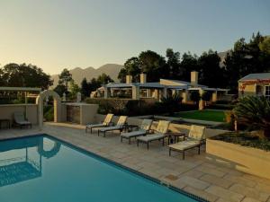 a backyard with a swimming pool with chairs and a house at La Cabriere Country House in Franschhoek