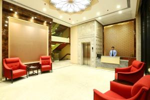 a lobby with red chairs and a man standing at a podium at Centrum Hotel by Brijwasi in Mathura