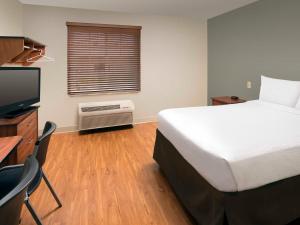 WoodSpring Suites Lincoln Northeast I-80 في لينكولن: غرفة نوم بسرير ومكتب وتلفزيون