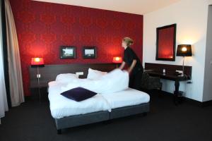 una mujer de pie junto a una cama en una habitación de hotel en Hotel Mijdrecht Marickenland, en Mijdrecht