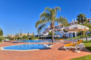 a resort with a swimming pool with chairs and an umbrella at Moradias Villas Rufino in Albufeira