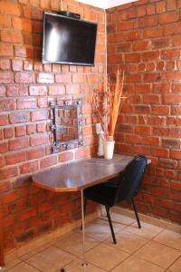 a brick wall with a table with a chair and a television at Pondoki Rest Camp in Groutfontein