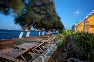 a row of benches next to the water with trees at Akti Naoussa Paros in Naousa