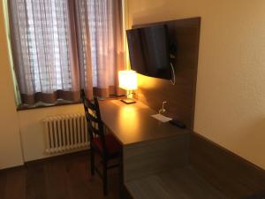 um quarto com uma secretária, uma televisão e um candeeiro em Zys Hotel em Wettingen