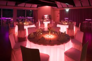 ein Zimmer mit weißen Tischen, Stühlen und lila Leuchten in der Unterkunft Parkhotel Hirschwang in Reichenau