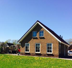a brick house with two windows and a grass field at Groepsaccomodatie Tzummarum in Tzummarum