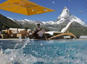 a woman sitting in a chair under an umbrella next to a pool at Riffelalp Resort 2222m in Zermatt