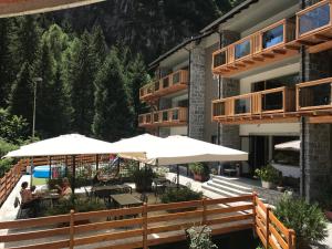 a hotel with tables and umbrellas in front of a building at Hotel Le Cime in Val Masino